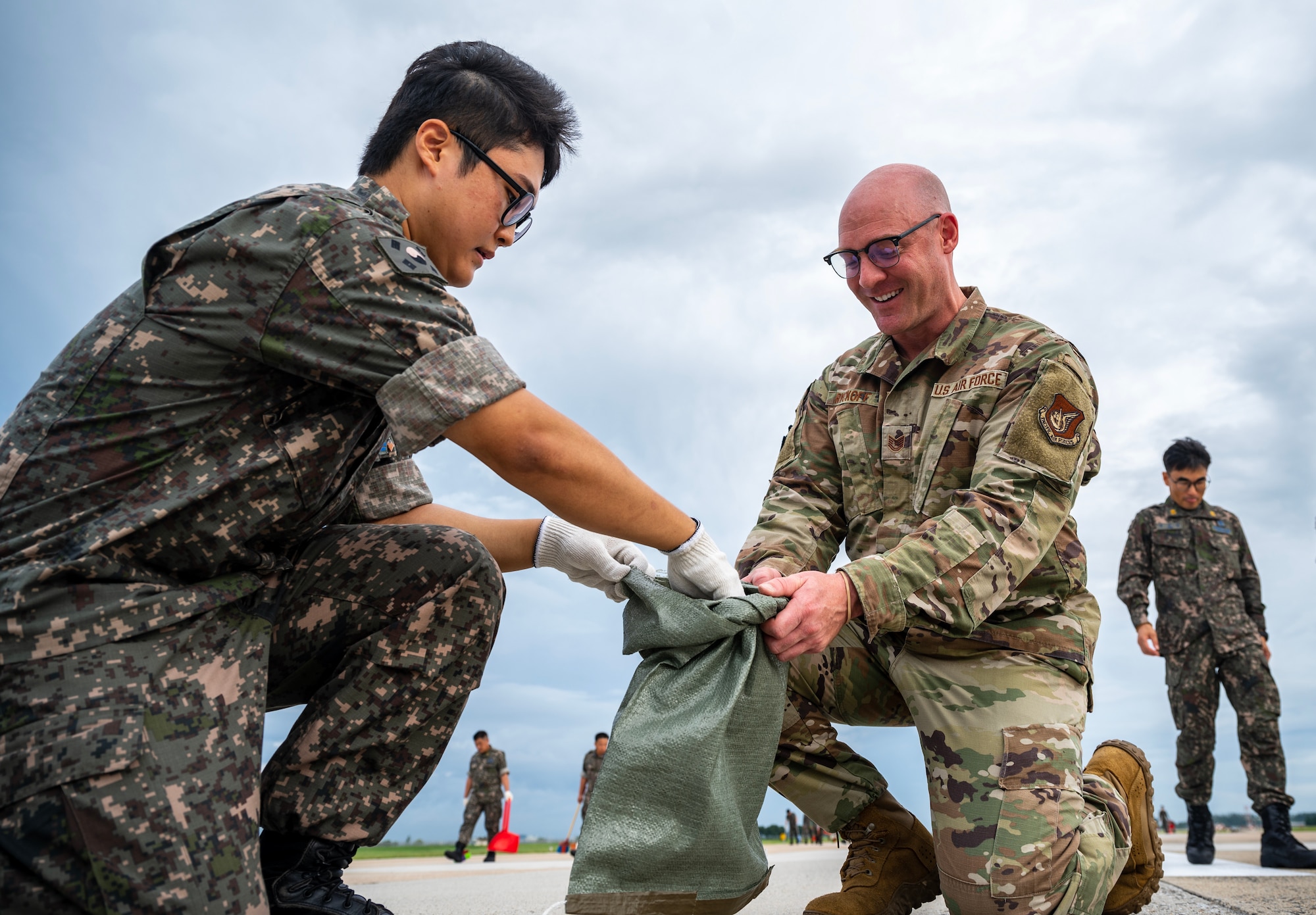 Tech. Sgt. Michael Ryckoff holds a trash bag for Airman 1st Class Kyle Lee during a foreign object debris inspection.