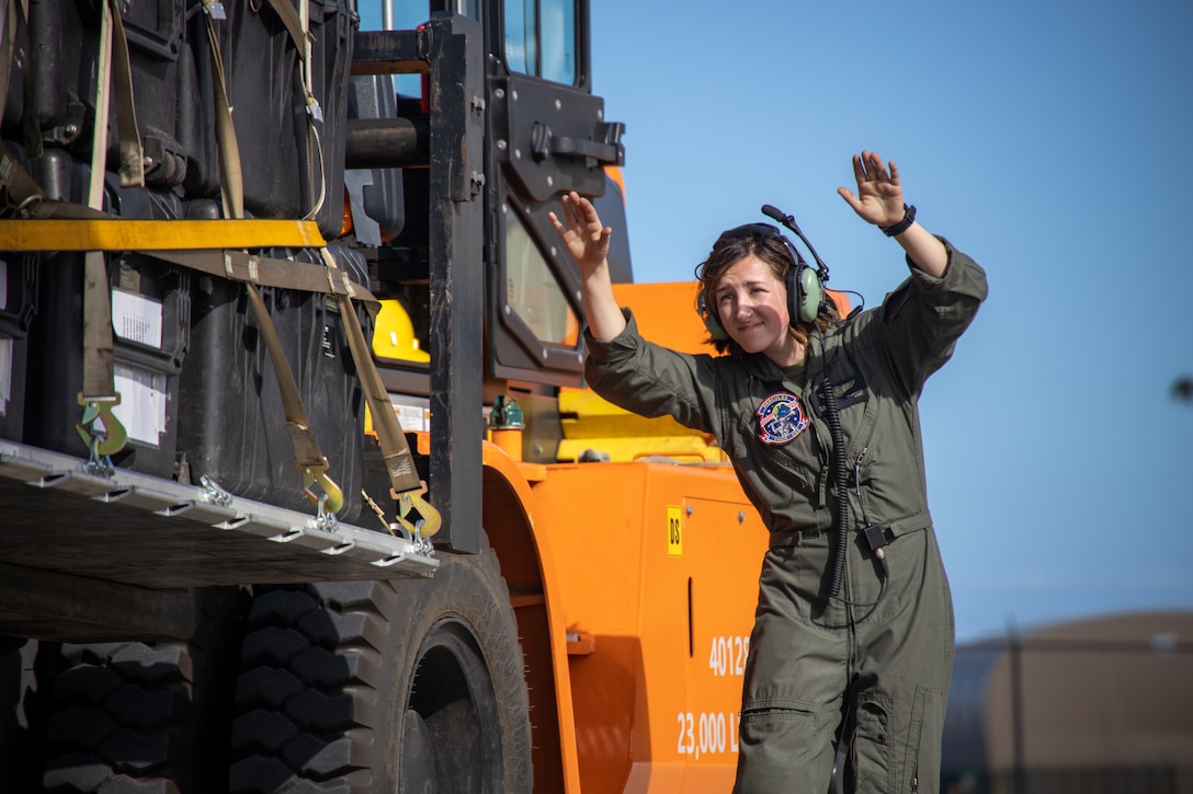 A Marine holds her arms in the air as she loads equipment into a plane.