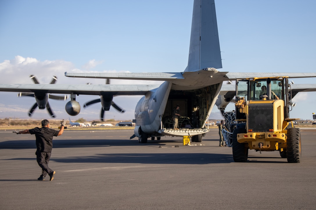 Marines unload supplies from the back of a large aircraft on a runway.