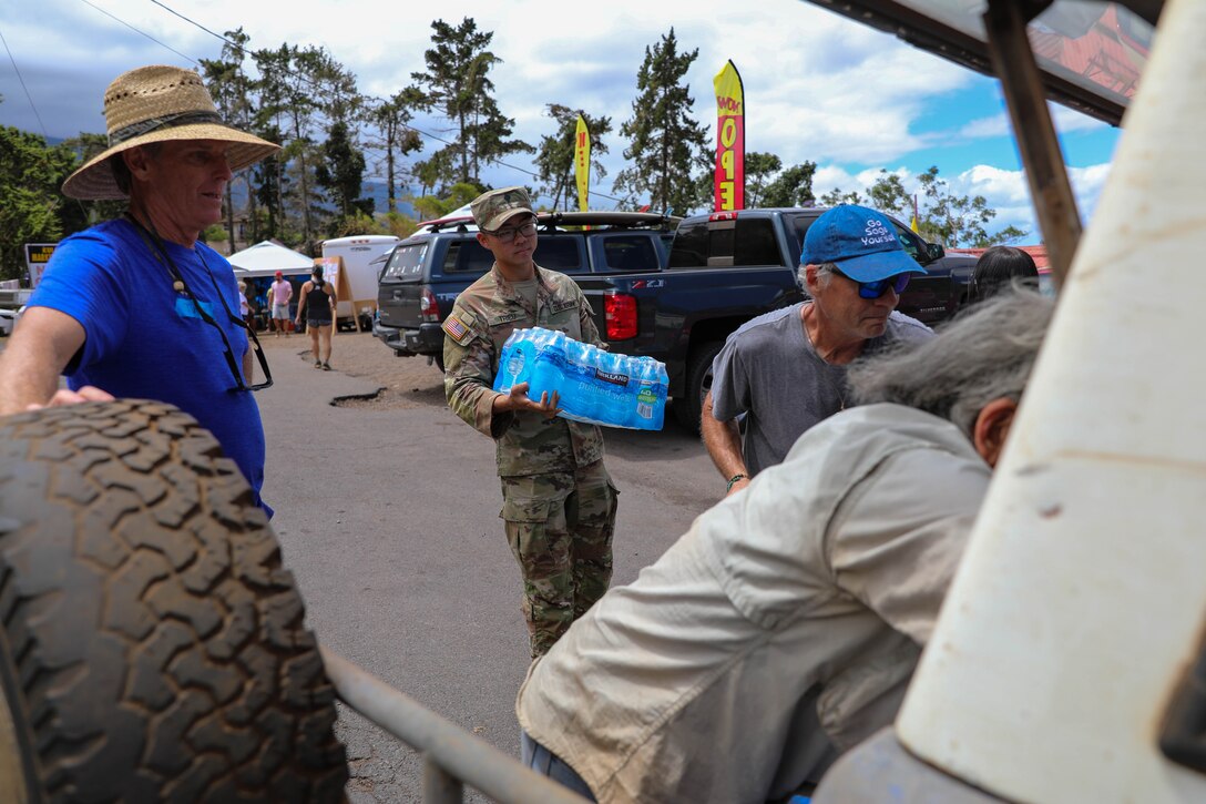 A National Guardsman carries a case of bottle water to people loading a car.