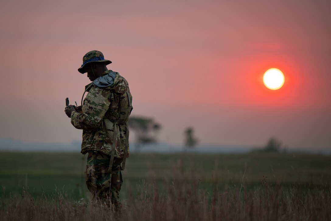 A soldier standing in a field at twilight checks his compass.