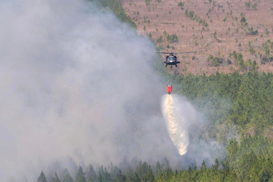 A helicopter uses a bambi bucket to drop water on a wildfire.