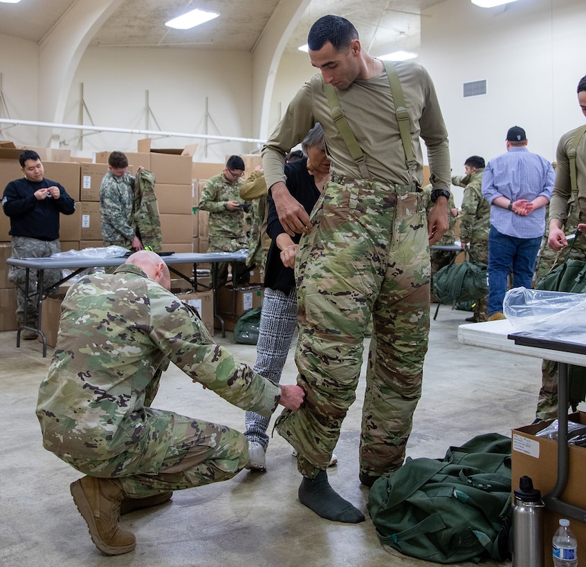 A soldier adjusts the fit of new cold weather clothing on another soldier.