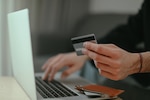 Person holding credit card next to laptop