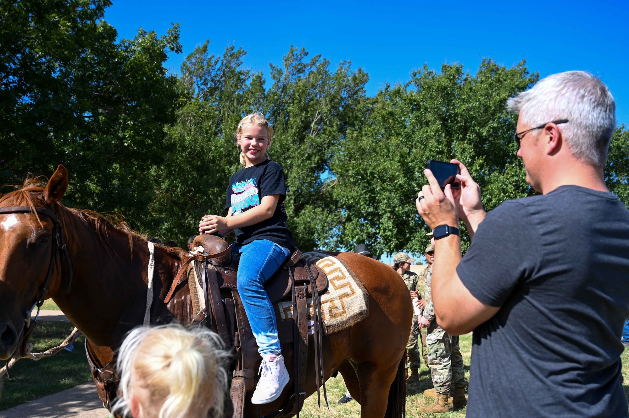 U.S. Air Force Maj. J.D. Oredson, 58th Airlift Squadron instructor pilot, takes a photo of his daughter, Phoebe, during the 25th Annual Cattle Drive at Altus Air Force Base (AFB), Oklahoma, Aug. 24, 2023. Altus AFB’s cattle drive started in 1999 when 15 riders and a herd of roughly 30 longhorn cattle paraded through the streets of Altus AFB. (U.S. Air Force photo by Airman 1st Class Kari Degraffenreed)