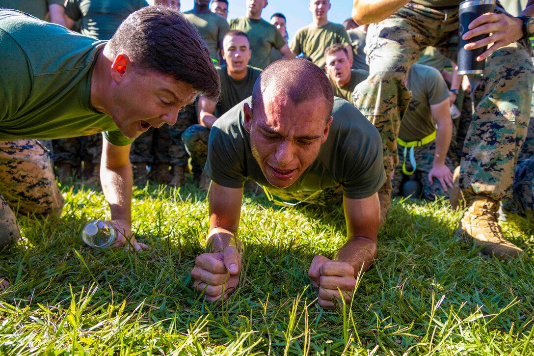 A Marine shouts at another Marine performing a plank as others surround them.