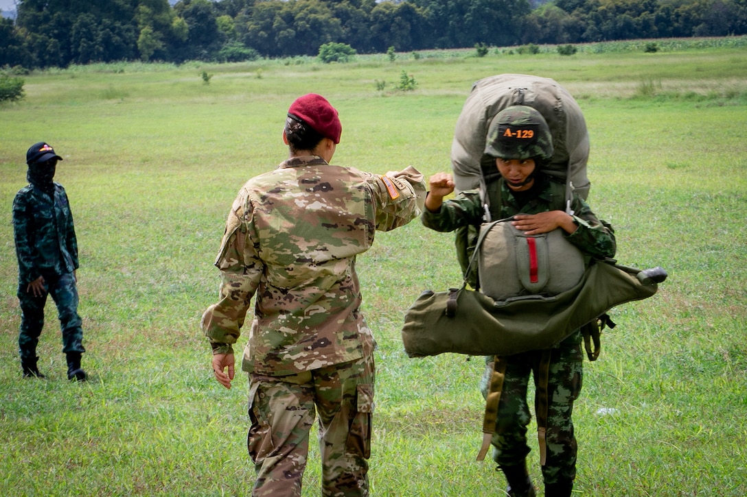 An American service member fist bumps a Thai service member on a grassy field during an airborne course.