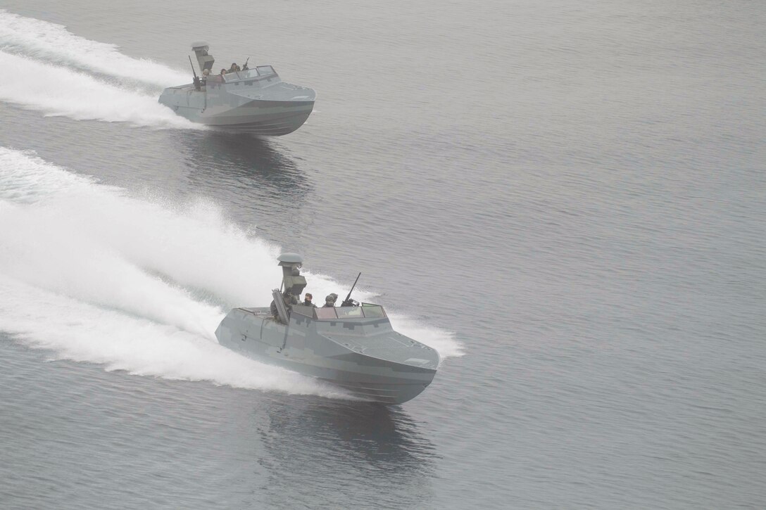 Sailors operate two boats in formation while carrying weapons.