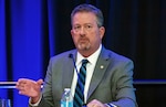 Head and shoulders picture of a white man speaking in front of a small microphone.