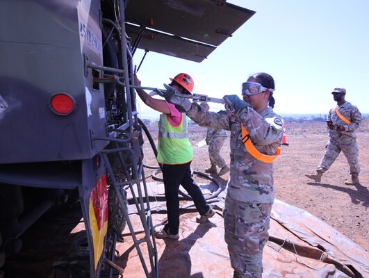A woman in an Army uniform returns a fuel line to a truck