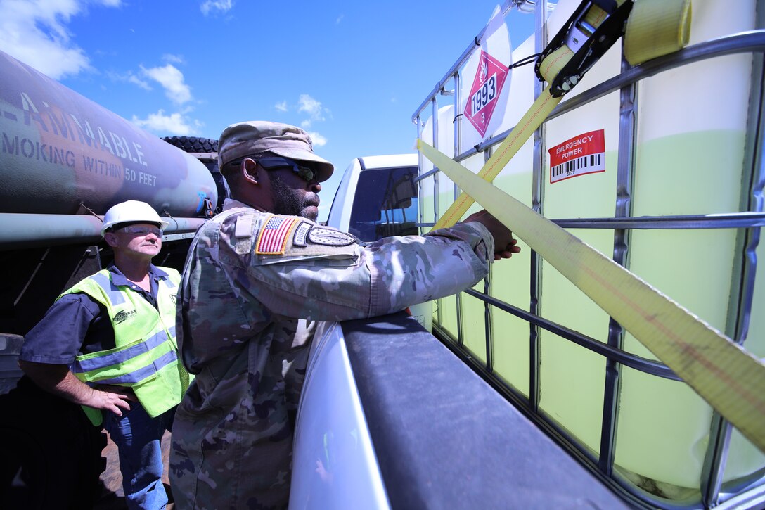 A man in an Army uniform secures a container of fuel while another man observes