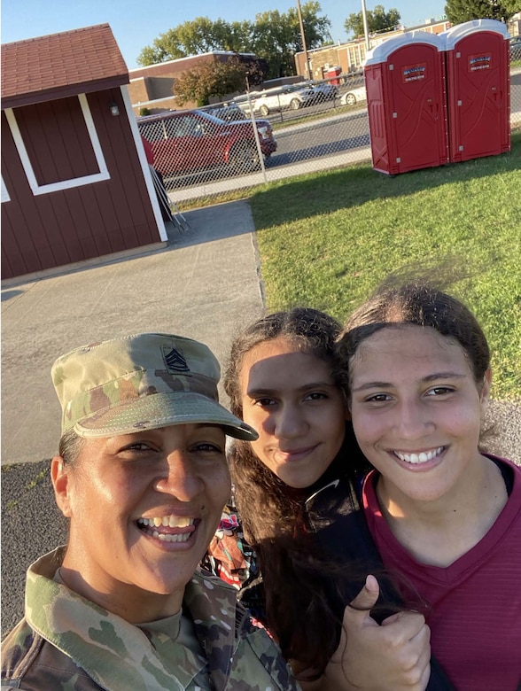 Female Soldier poses with two girls outside.
