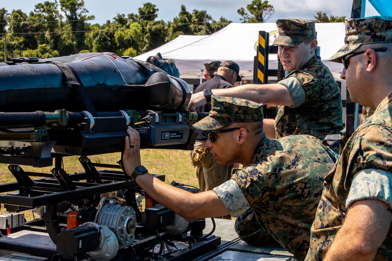 Three service members work outdoors with a large piece of equipment.