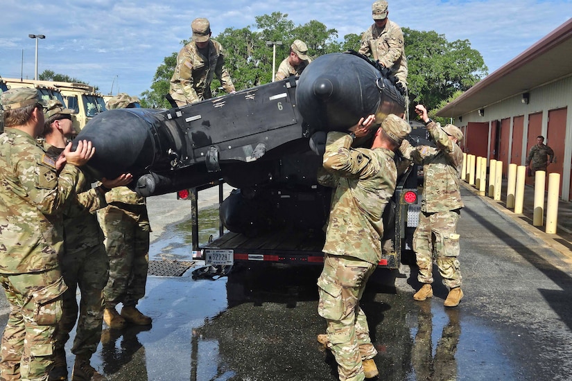People in military uniform hoist a rubber boat from a trailer.