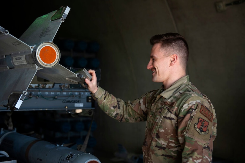 A man in military uniform adjusts the tail fin of a missile.