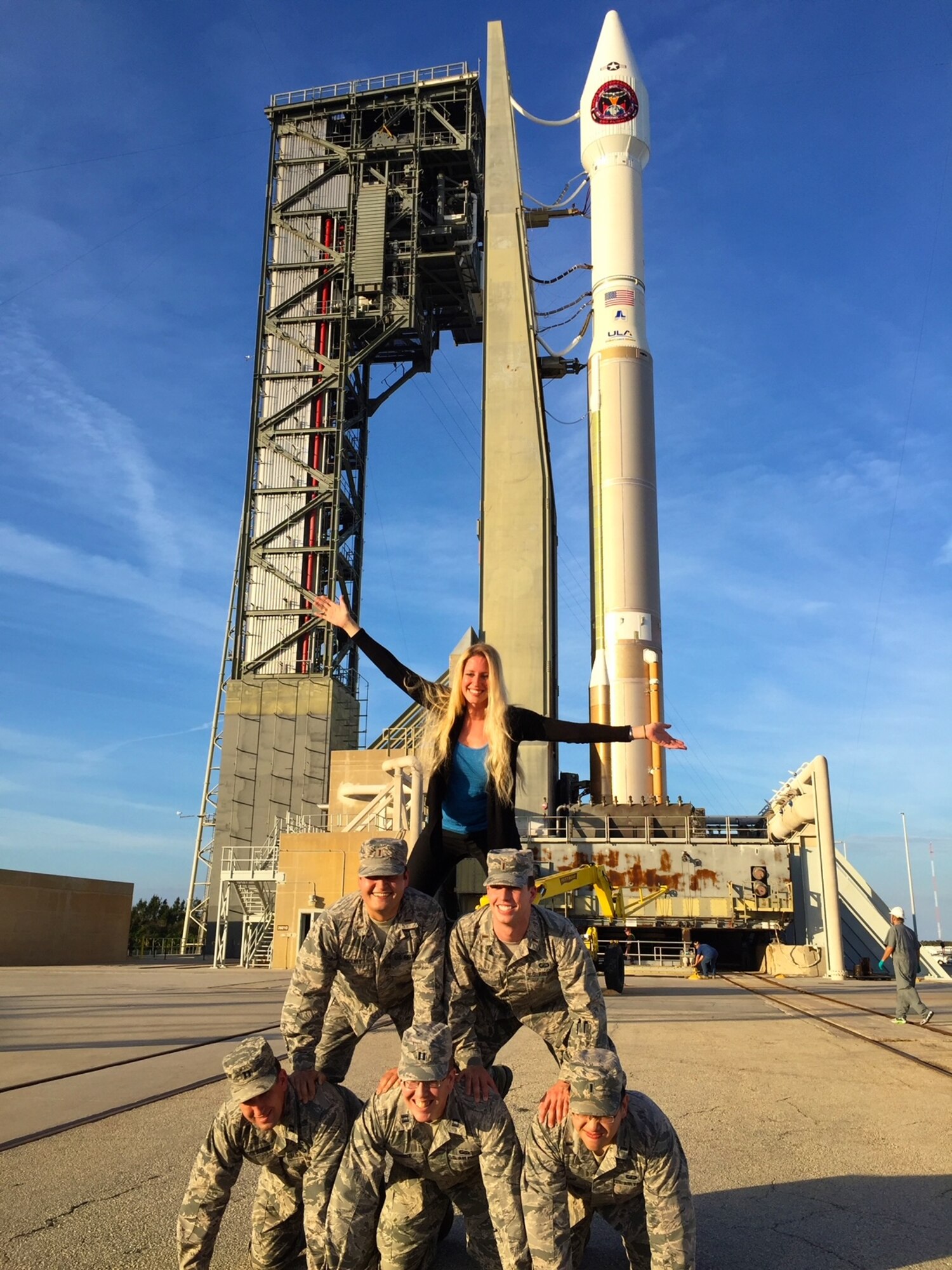 Military members in uniform make human a pyramid in front of a space rocket