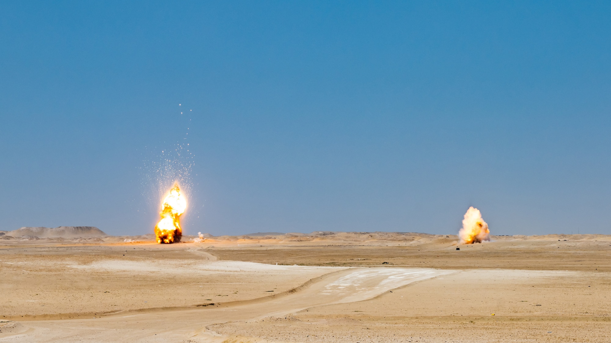 Two explosions rise in the distance as part of a large-scale detonation during Operation Solar Flare at Udairi Range, Kuwait, Aug. 24, 2023. Solar Flare is a 5-day, joint-service field training exercise developed and hosted by the 386th and 332nd Expeditionary Civil Engineer Squadron’s EOD teams that brought together 30 Army, Navy, and Air Force personnel for a series of intense training scenarios focused on working together through current and emerging threats in the CENTCOM AOR. (U.S. Air Force photo by Staff Sgt. Kevin Long)