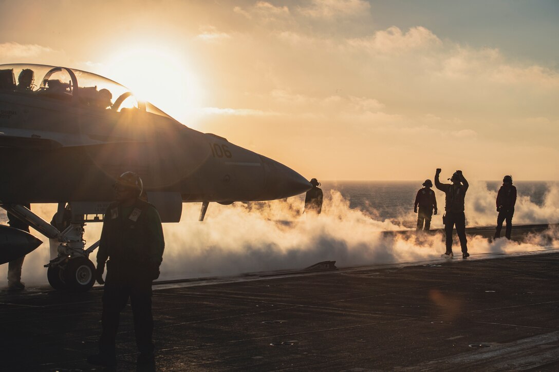 A fighter jet prepares to take off from a ship at sea at twilight.