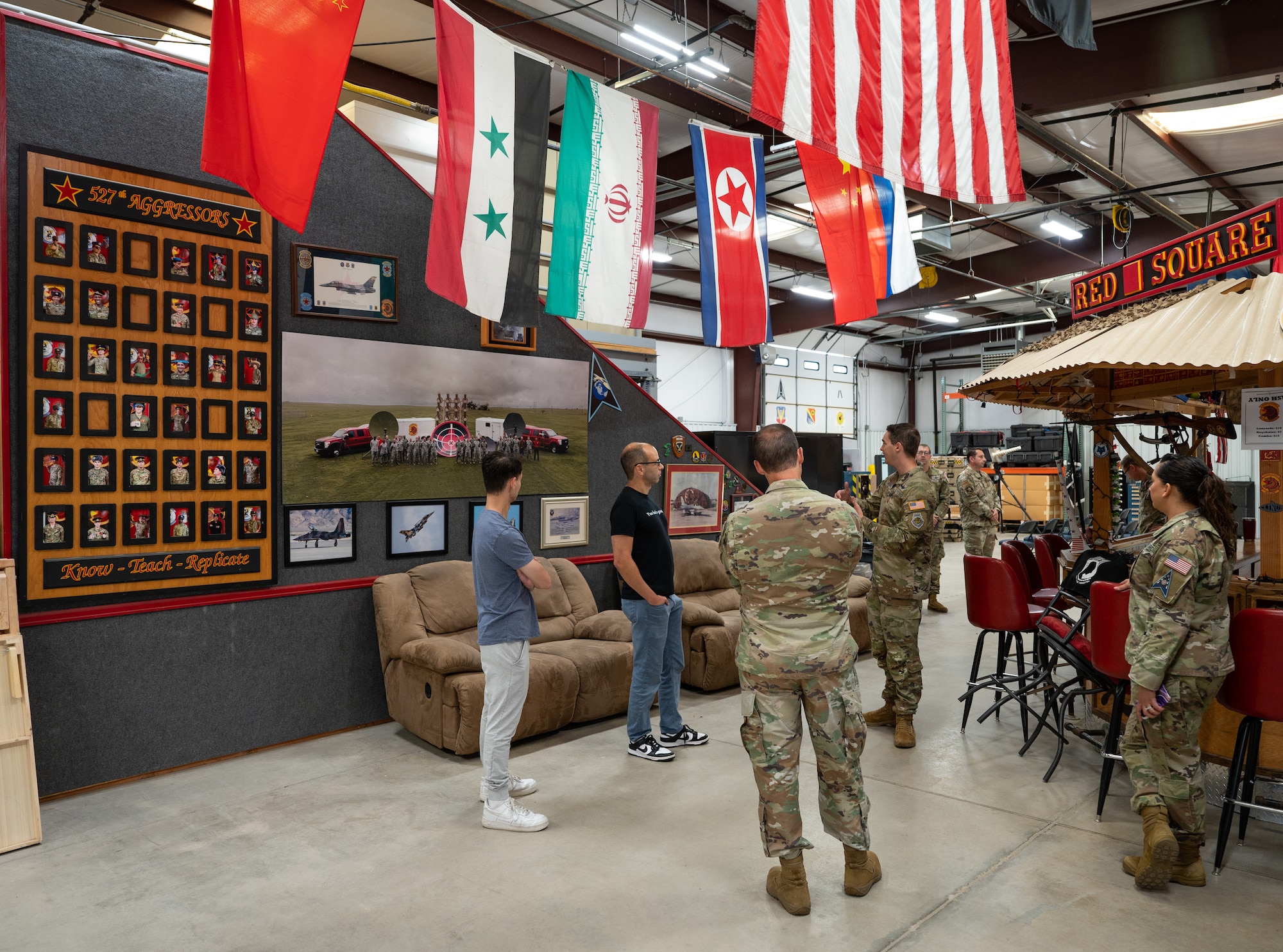 James Murray and U.S. Space Force 527th Space Aggressor Squadron service members stand in their workspace with adversarial flags hanging above them.