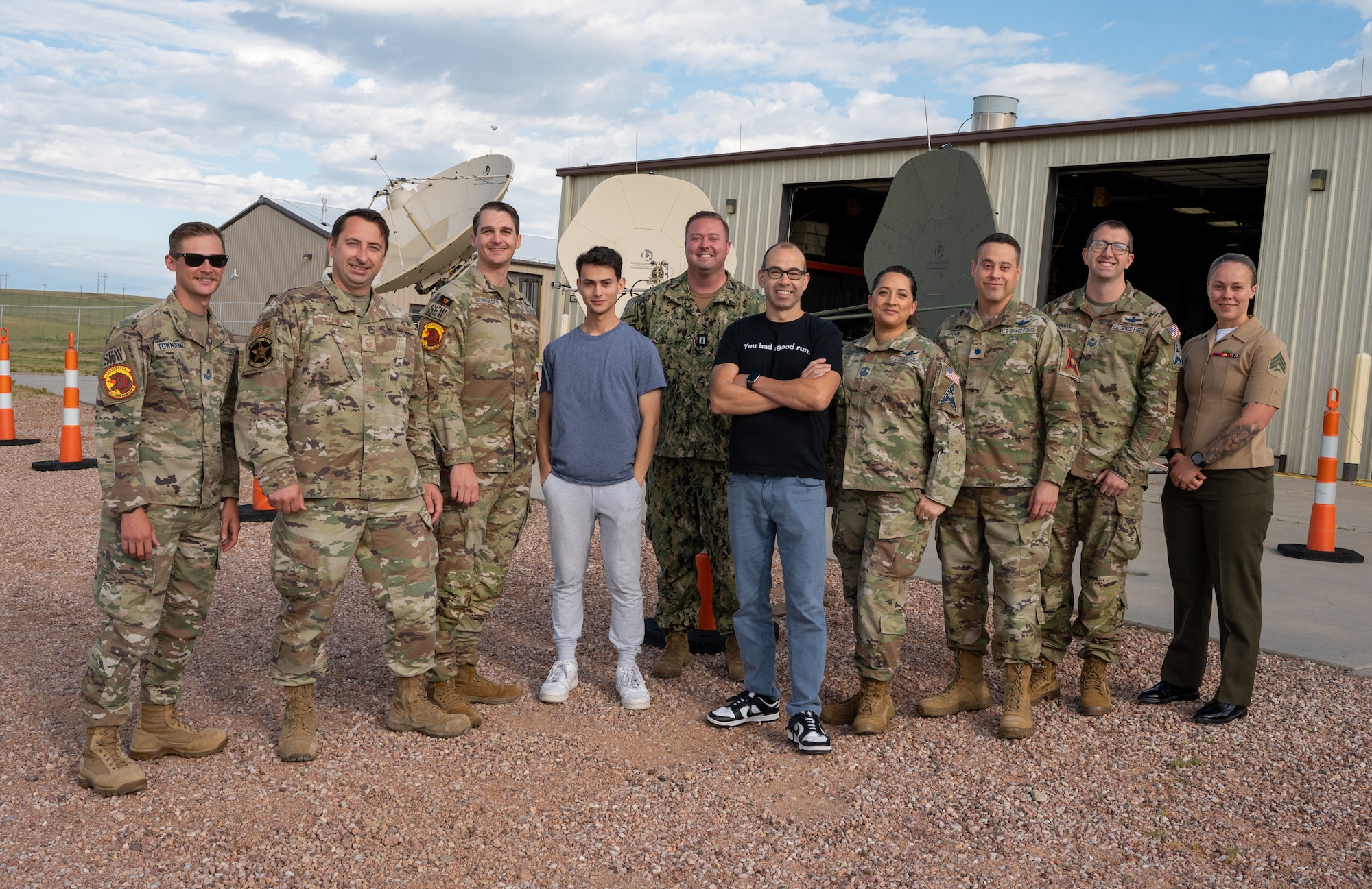 James Murray and a group of U.S. service members with the 527th Space Aggressor Squadron pose for a photo in front of satellite dishes.