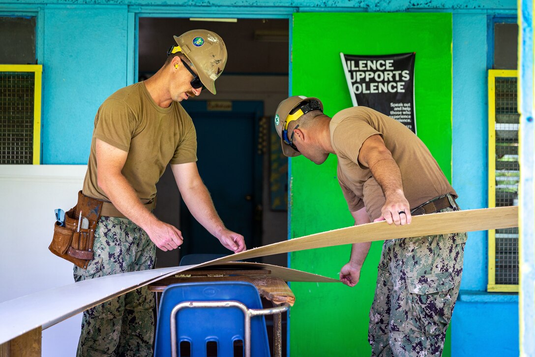 Sailors work on the wall of a building during a renovation project.