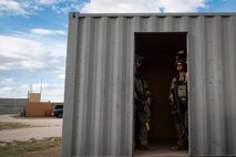 Two uniformed military members stand in the doorway of a cargo container.