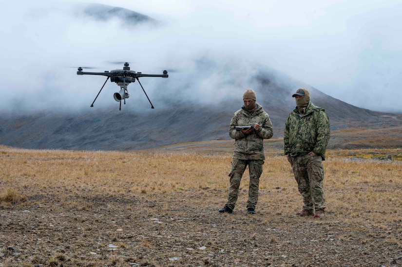 A drone hovers near two men in uniform.