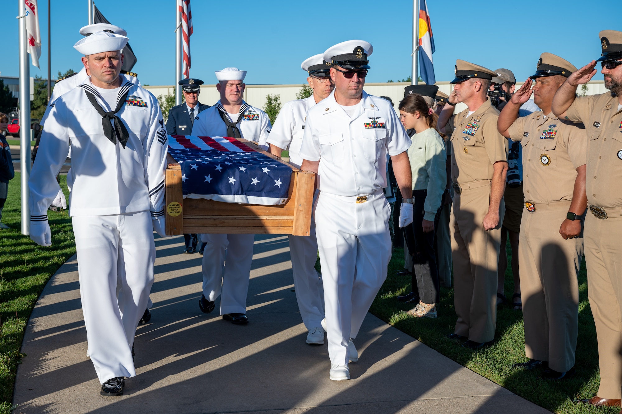 Sailors carry a wooden box with an American flag on top.