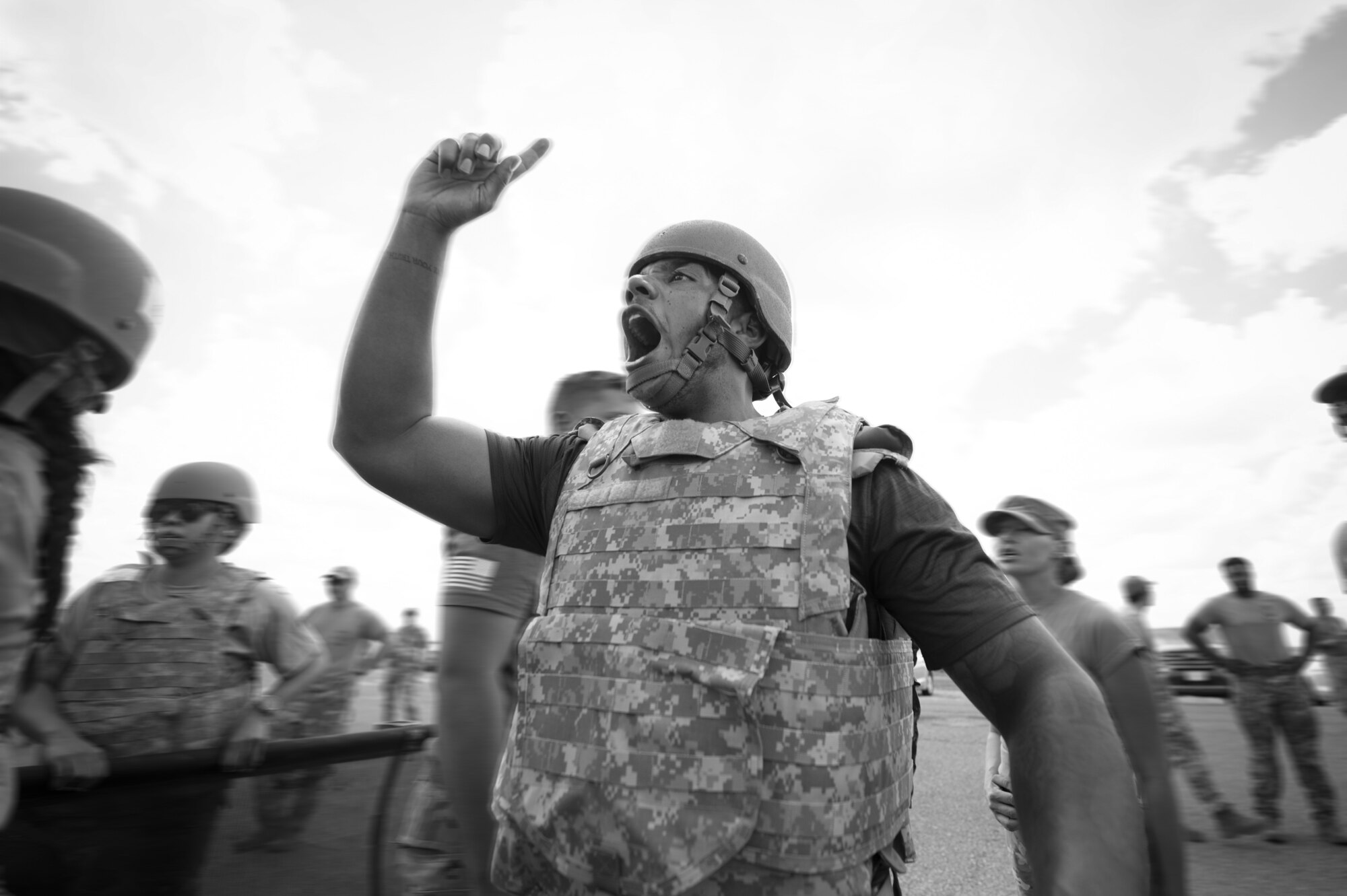 A black-and-white image shows a man in a tactical vest and helmet yelling.