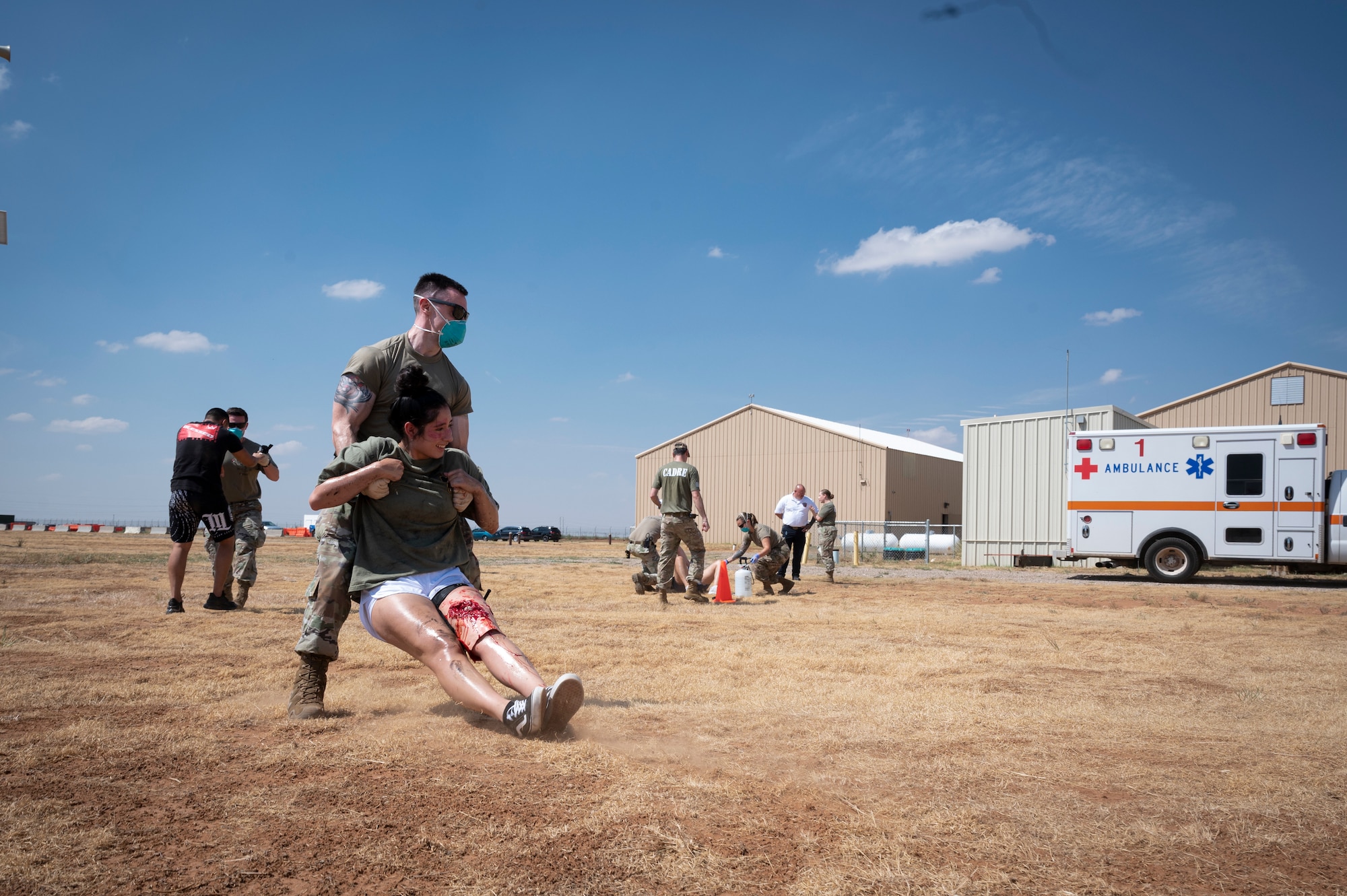 Medics evacuate simulated patients in a field toward an ambulance in the background.