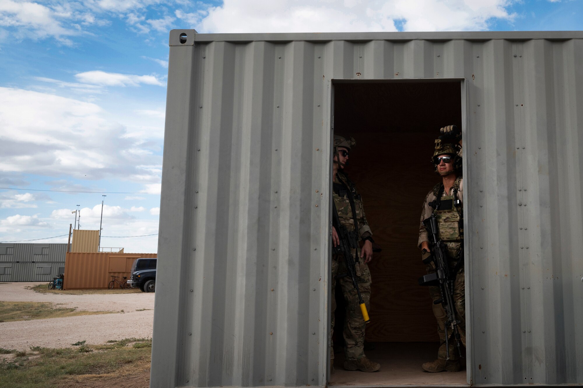 Two uniformed military members stand in the doorway of a cargo container.