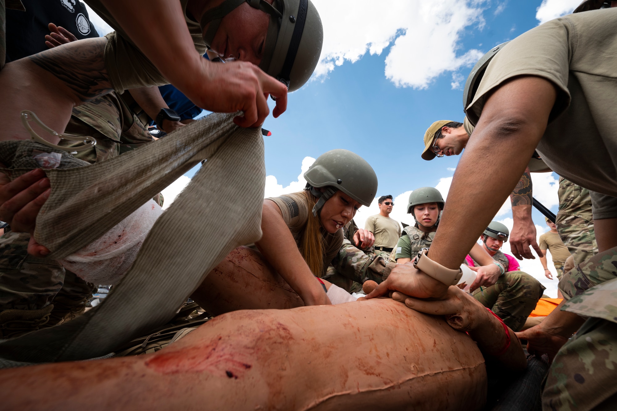 A group of people in helmets and tactical vests apply pressure to a medical mannequin's leg to stop simulated bleeding.