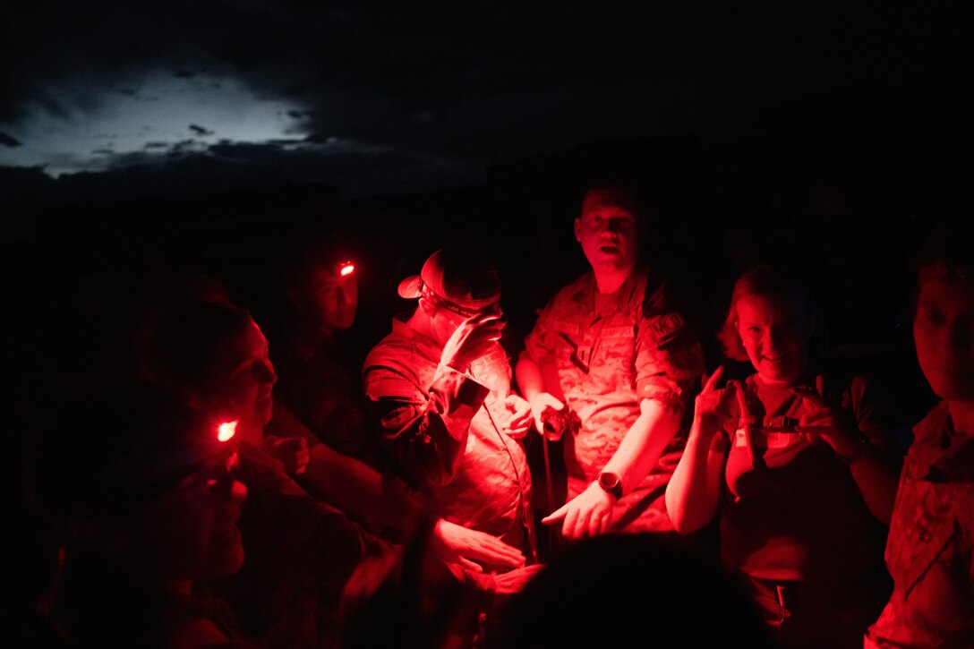 A group of Airmen gathered in a circle at night illuminated by the red glow of a tactical light.