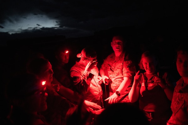 A group of Airmen gathered in a circle at night illuminated by the red glow of a tactical light.