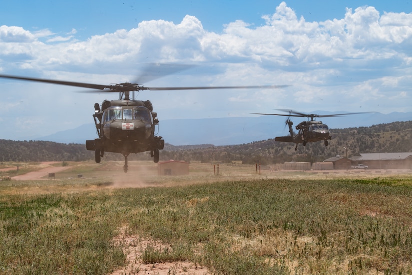Two helicopters hovering low to the ground in a field preparing to land.