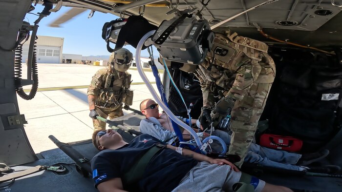 From the perspective of inside a helicopter, two Soldiers with flight helmets looking over two patients in litters, preparing to offload them.