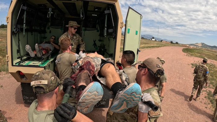 A group of servicemembers loading a patient in a litter into the rear compartment of a truck with one patient already inside.