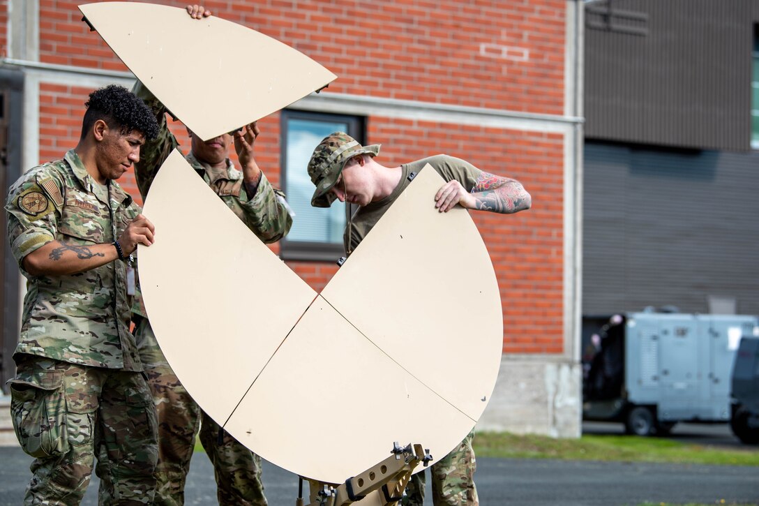 Three airman assemble a satellite dish.