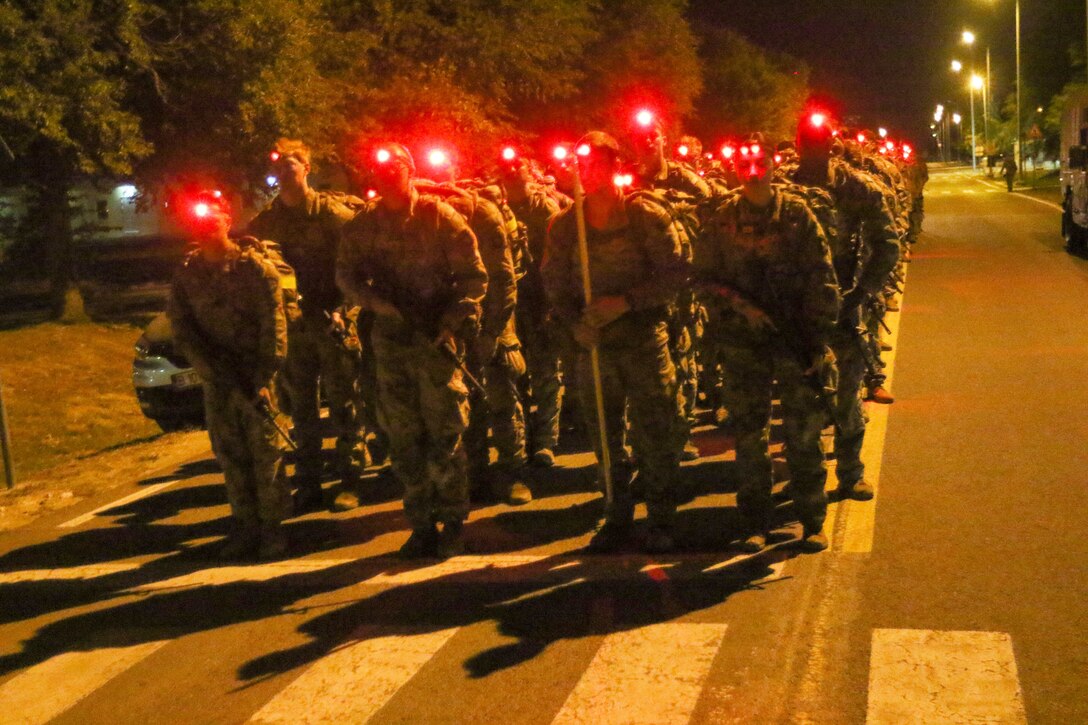 A group of soldiers wearing headlamps stand in a road.