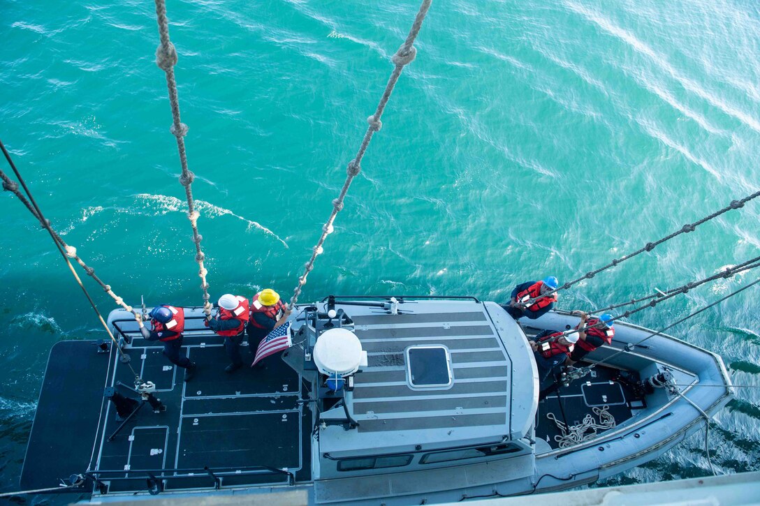 Sailors use ropes to lower a small boat into the water.