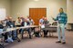 A person speaks to a group of people seated at tables.