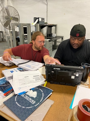 Man with paperwork points at computer screen while another man inputs data