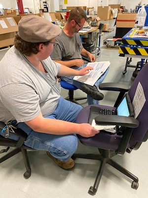 Man sits in a mobile office on a computer while going over paperwork with another man