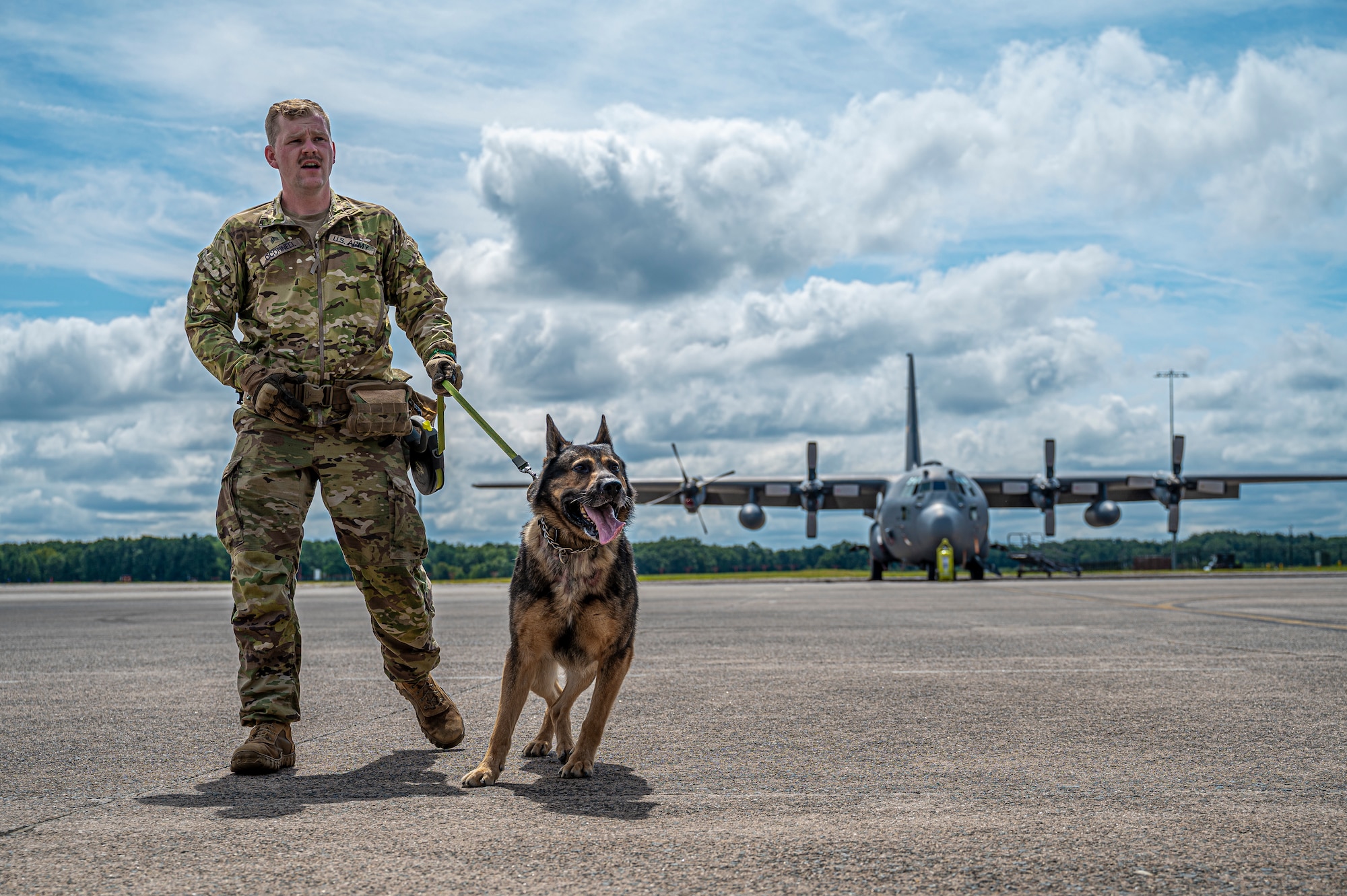 U.S. Army Sgt. Kevin O'Connell and his working dog, Misha, walk across the tarmac of Bradley Air National Guard Base in East Granby, Conn., to investigate a C-130H aircraft as part of a training exercise Aug. 29, 2023. This training was designed to help handlers and their K-9 step outside their comfort zone, train in an unfamiliar environment, and build rapport with their sister service.
