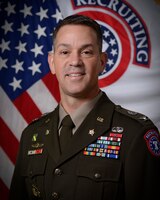 man wearing u.s. army uniform standing in front of two flags.