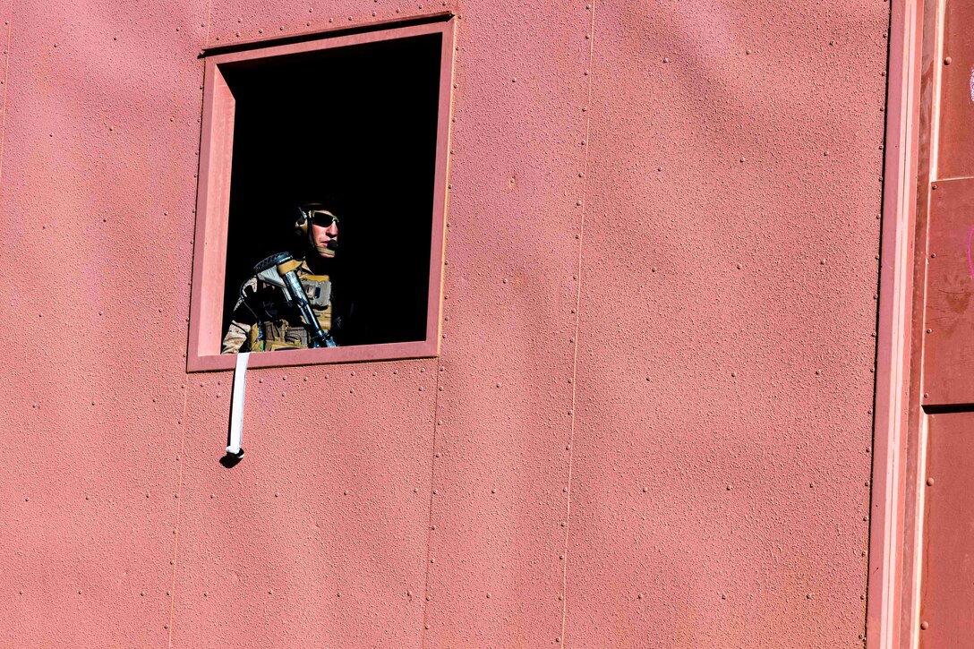 A Marine partially covered by shadows looks out of a window.