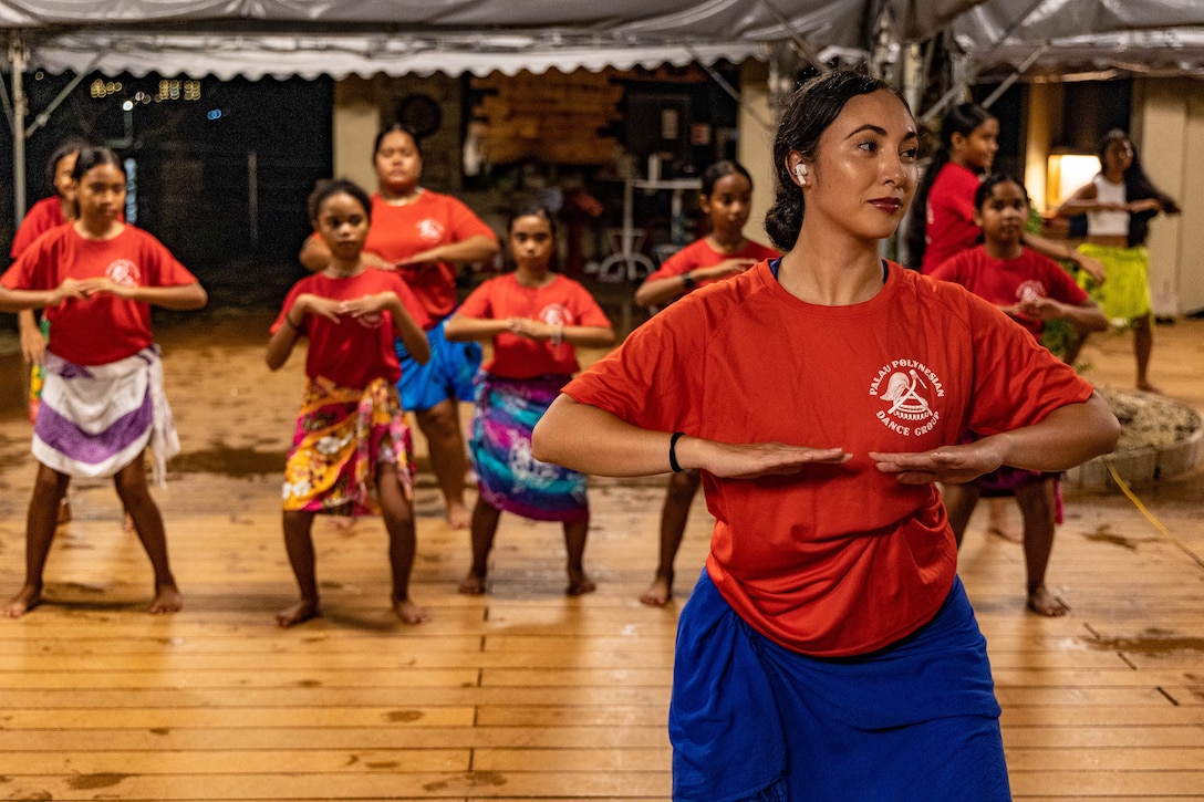 A service member shows a dance move as children perform the same movement in the background.