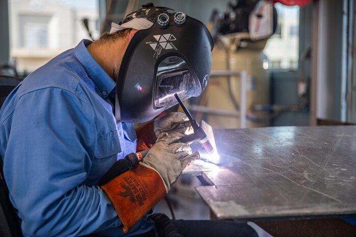 A person in a blue shirt is welding aluminum