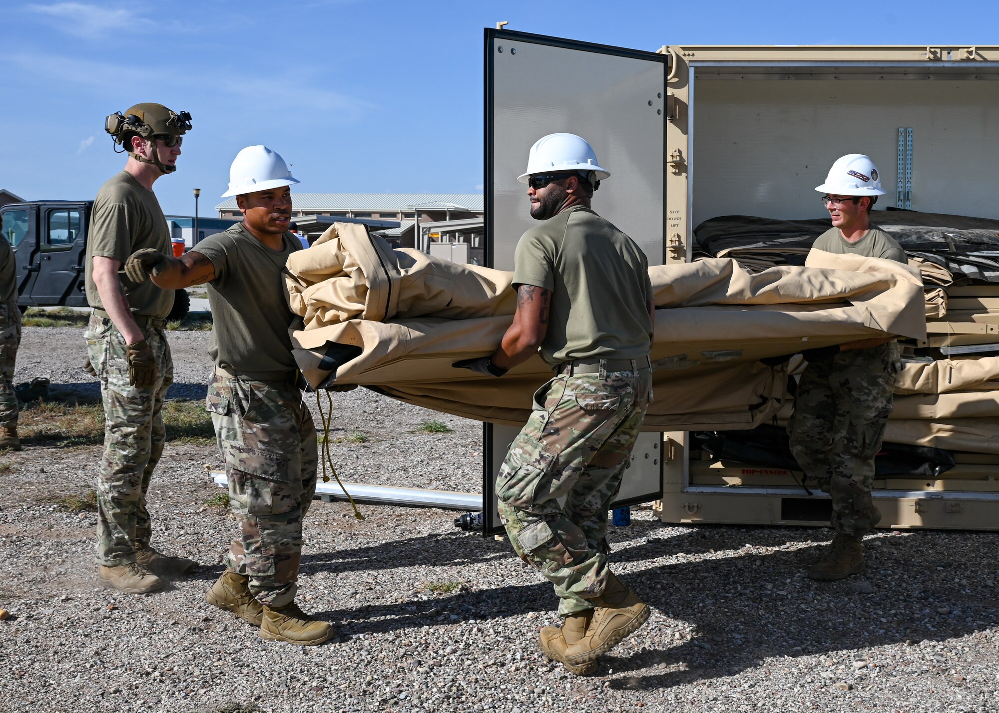 A photo of people in military uniforms and hard hats moving a piece of a large tent.