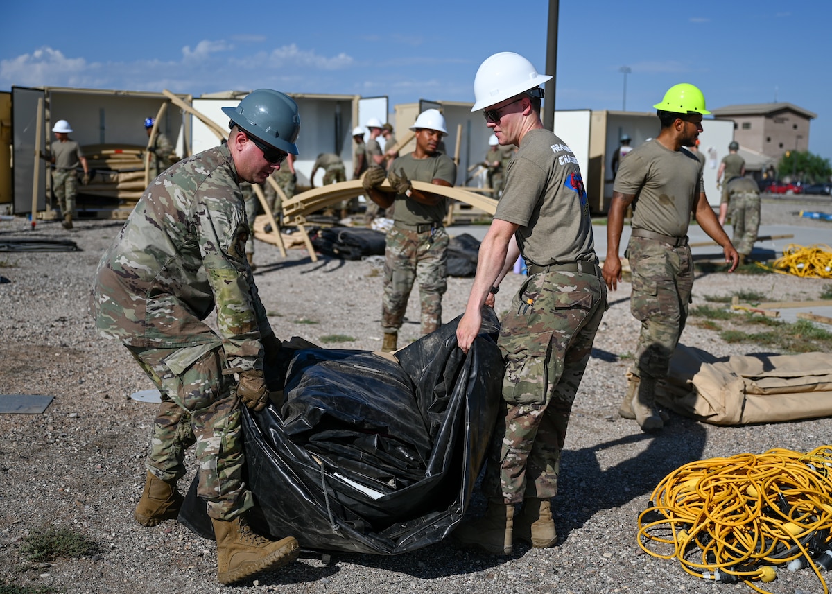 A photo of people in military uniforms and hard hats moving a large black tarp.